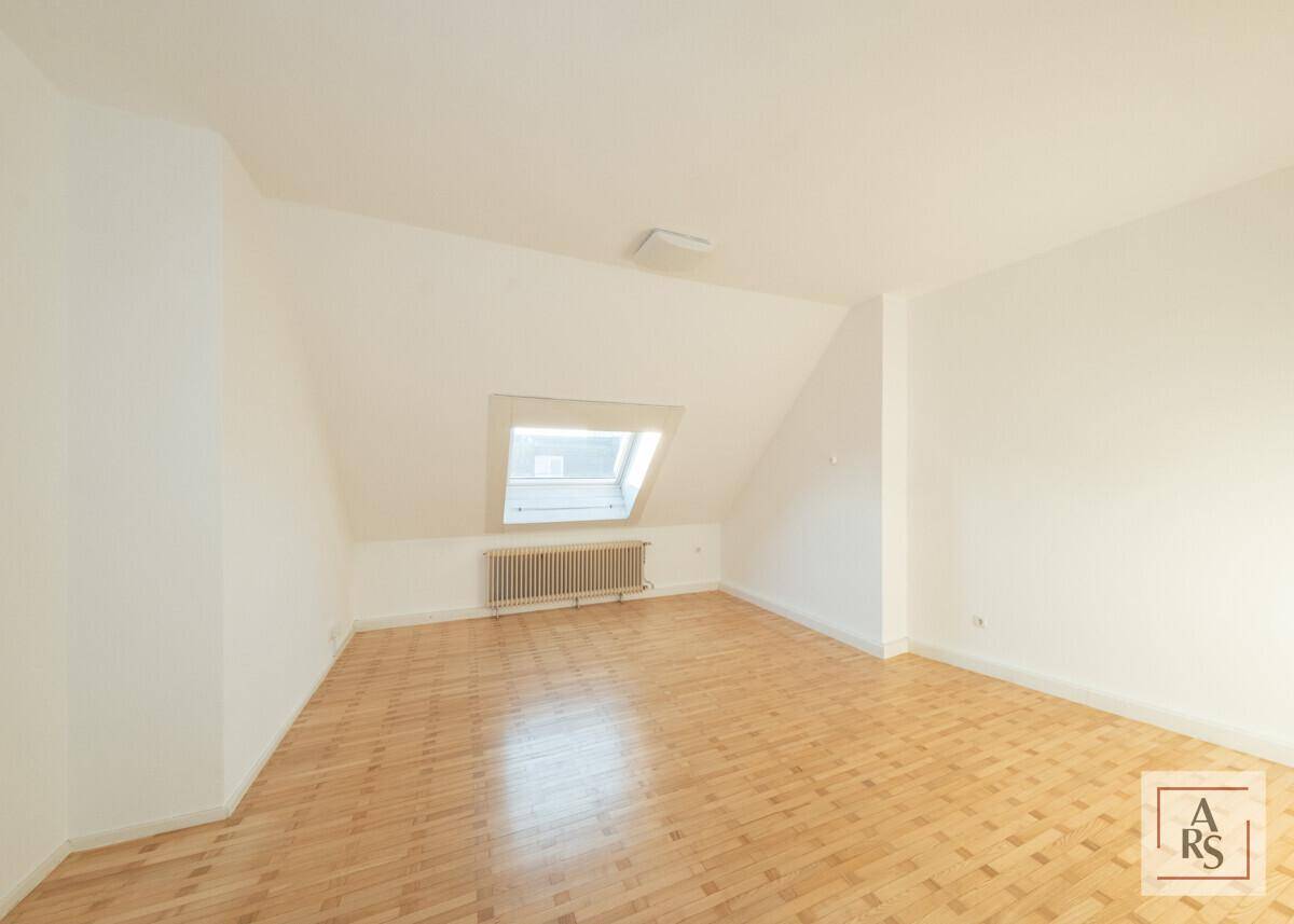 Dachzimmer mit schrägen Wänden, Parkettboden und einem Dachfenster für natürliches Licht.