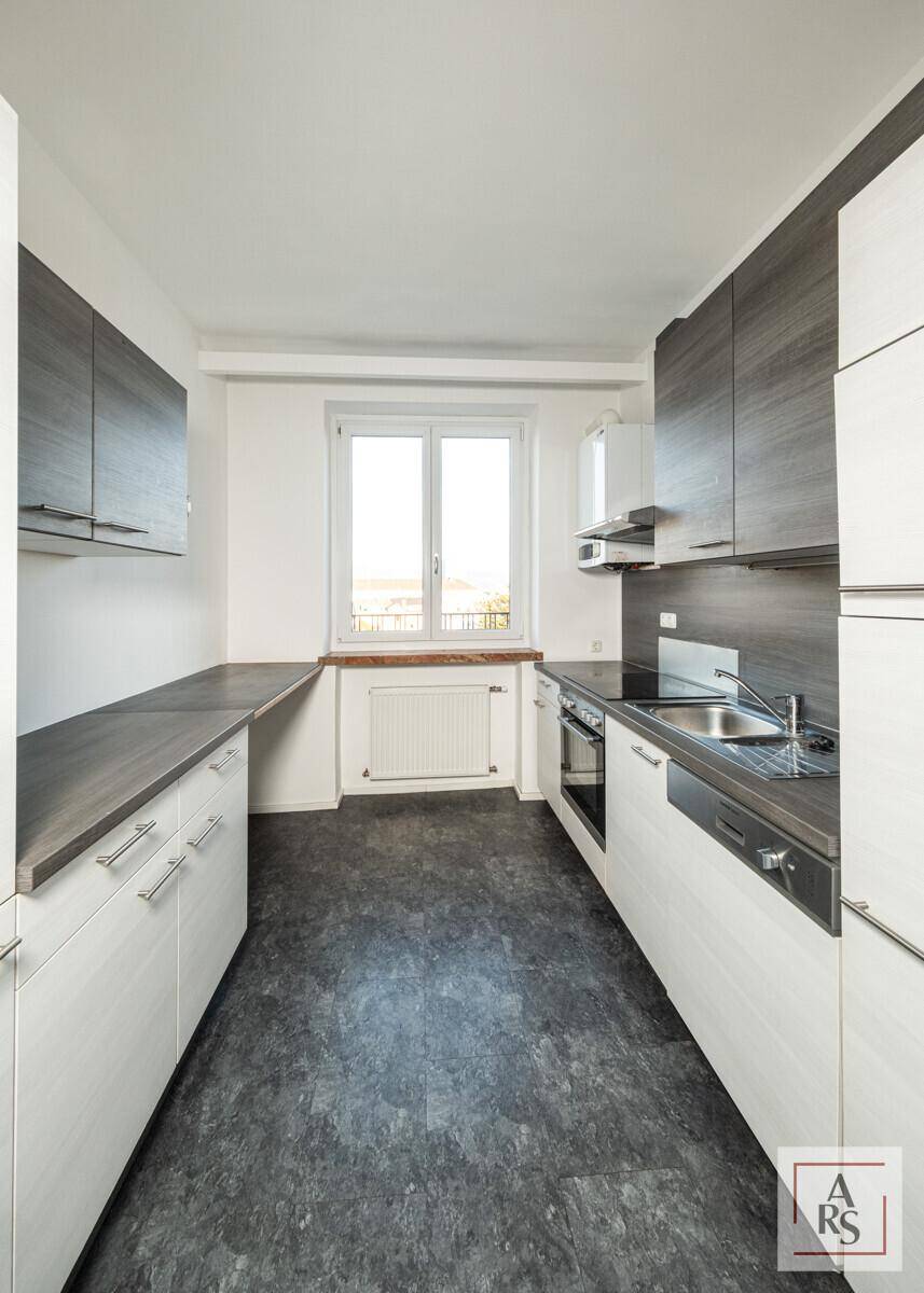 Funktionale Küche mit weißen und grauen Schränken, Fenster und integrierten Geräten.