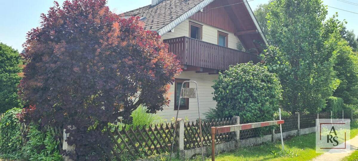 Charmantes Einfamilienhaus mit Holzbalkon und umzäuntem Vorgarten in grüner Umgebung.