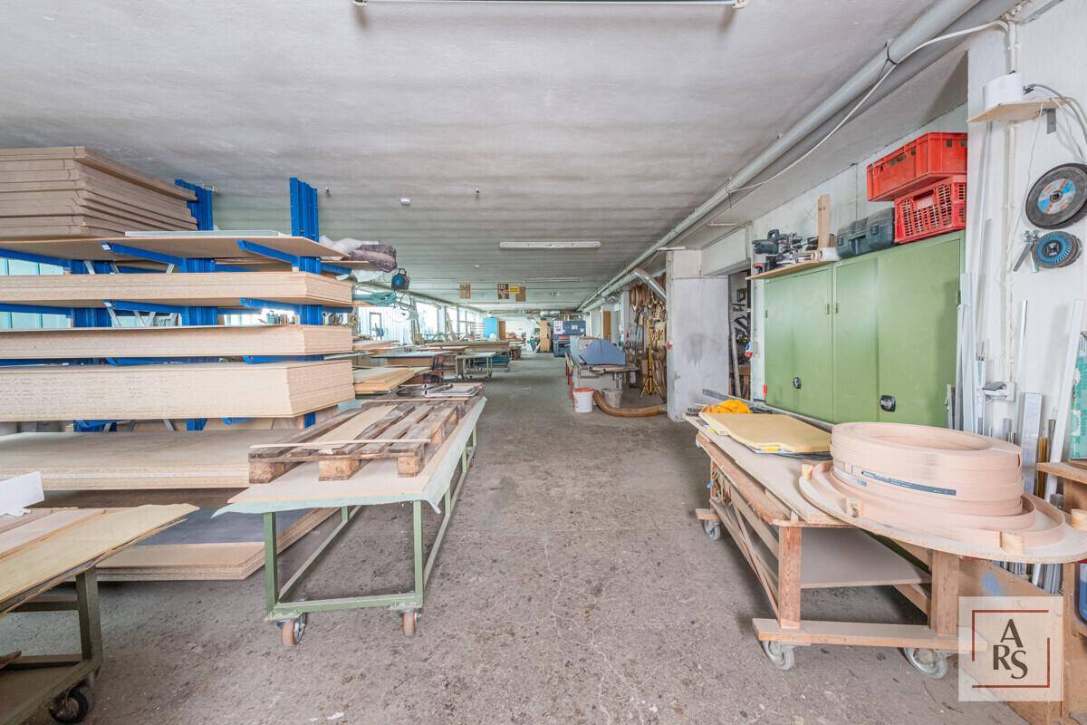 Langer Werkstattbereich mit Holzmaterialien auf Regalen und Arbeitstischen, bereit zur Bearbeitung und Lagerung.