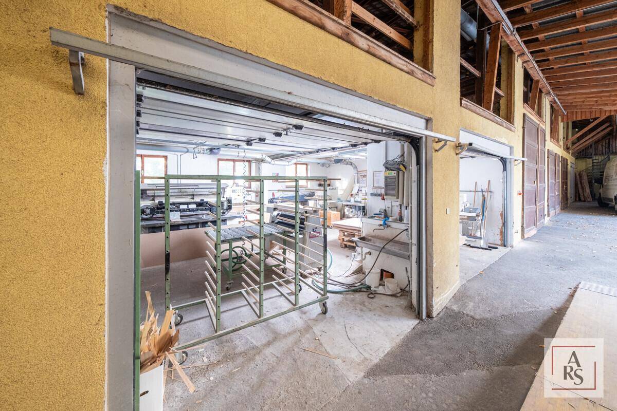 Blick aus einem großen Garagentor in einen hellen Werkstattbereich mit Maschinen und Regalen, gut beleuchtet.