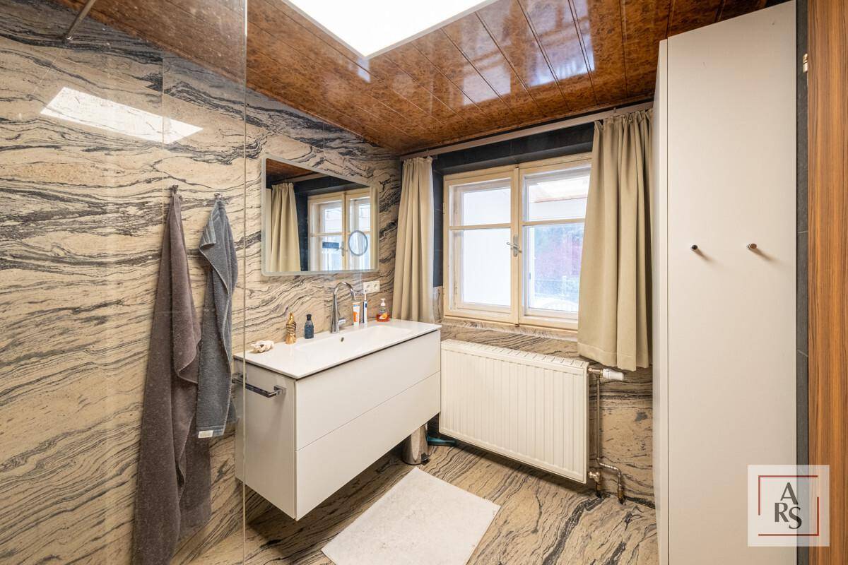 Modernes Badezimmer mit auffälligen Marmorfliesen, Fenster und einem schwebenden Waschtisch.