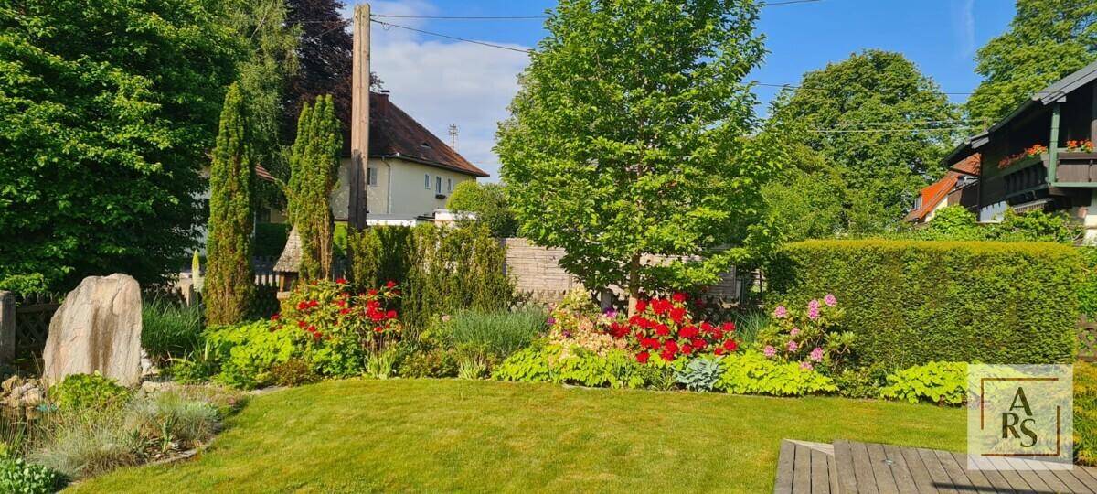 Idyllischer Gartenbereich mit blühenden Sträuchern, Rasen und einer kleinen Holzterrasse.