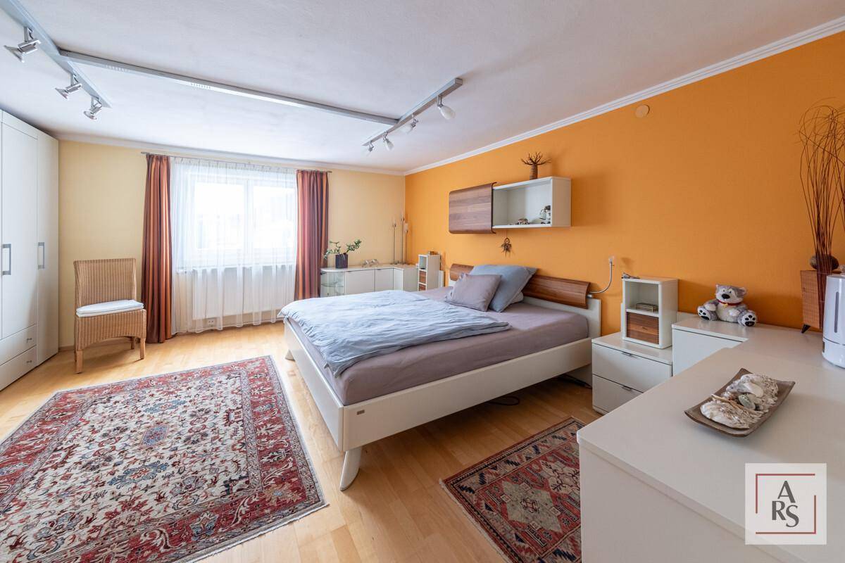 Helles Schlafzimmer mit orangefarbener Akzentwand, Parkettboden und großem Bett.