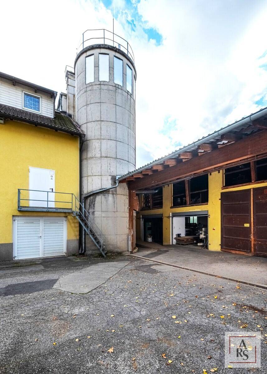 Außenansicht eines Gebäudekomplexes mit einem markanten Betonturm und großen Garagentoren im Hofbereich.
