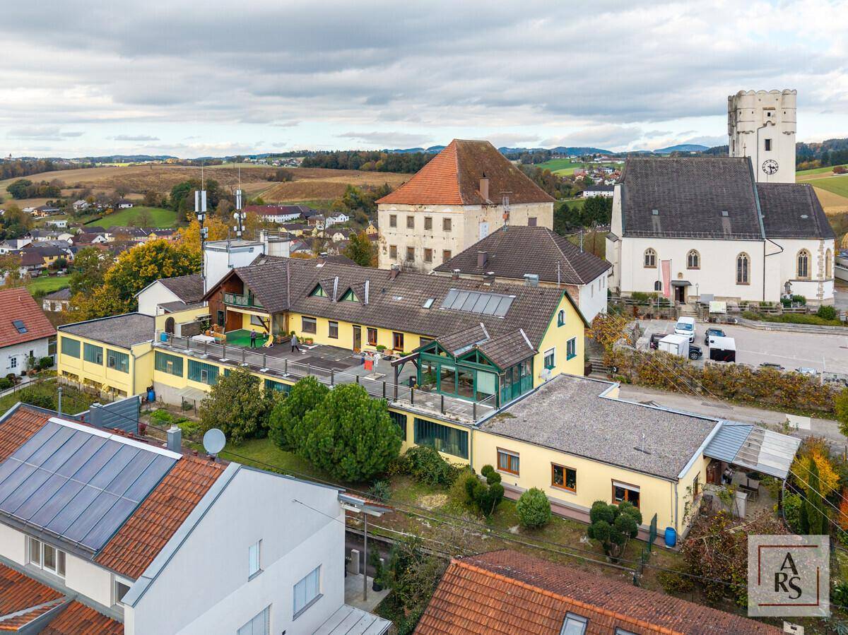 Luftaufnahme einer ländlichen Stadt mit mehreren Gebäuden, darunter eine Kirche und ein Schloss, umgeben von Natur.