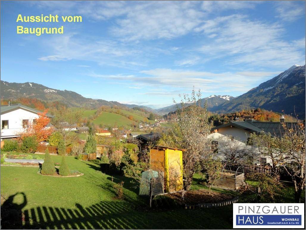 Gartenbereich mit Blick auf die umliegende Berglandschaft und weitere Häuser unter blauem Himmel.