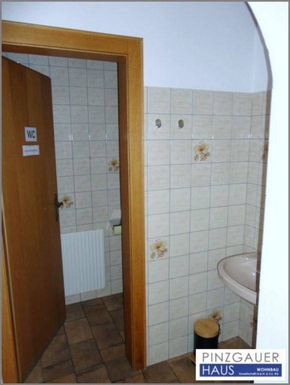 Einfaches Gäste-WC mit beigefarbenen Fliesen, einem kleinen Waschbecken und einer Holztür.
