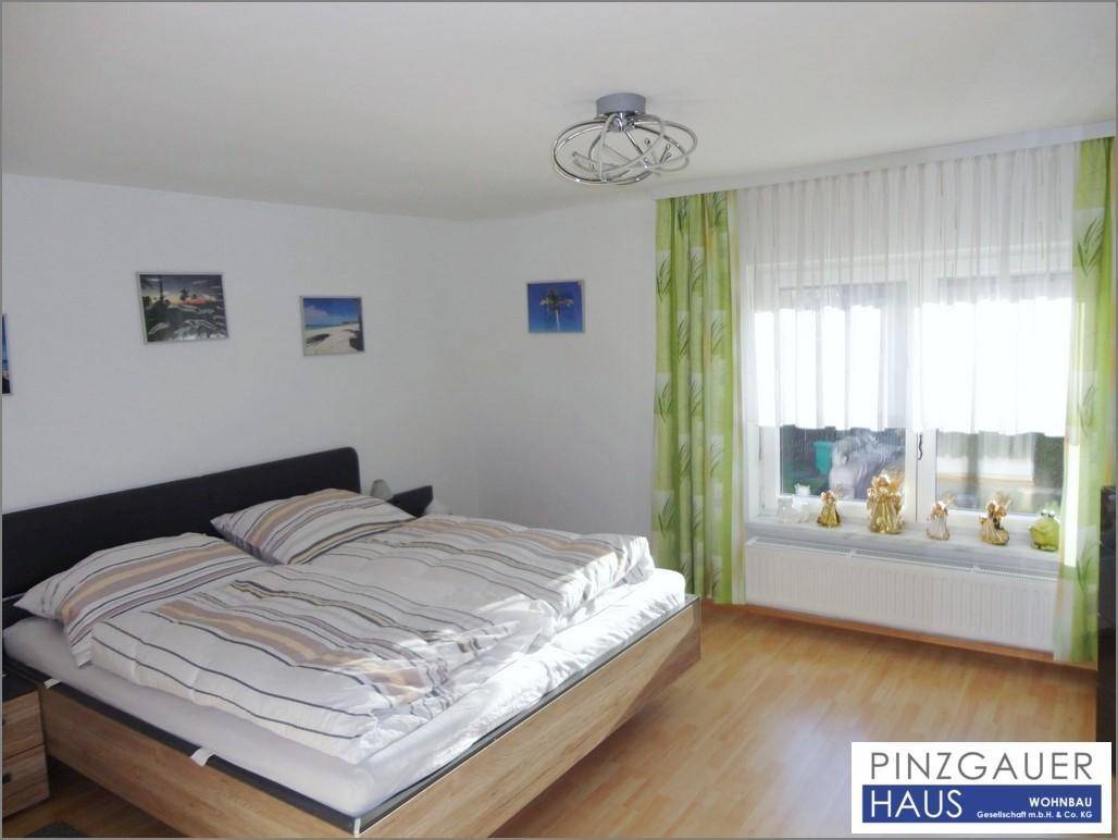 Helles Schlafzimmer mit Doppelbett, Laminatboden und Fenster mit grünen Vorhängen.