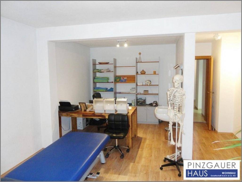 Funktional eingerichtetes Büro mit Schreibtisch, Regalen und einer Behandlungsliege, ideal für eine Praxis.