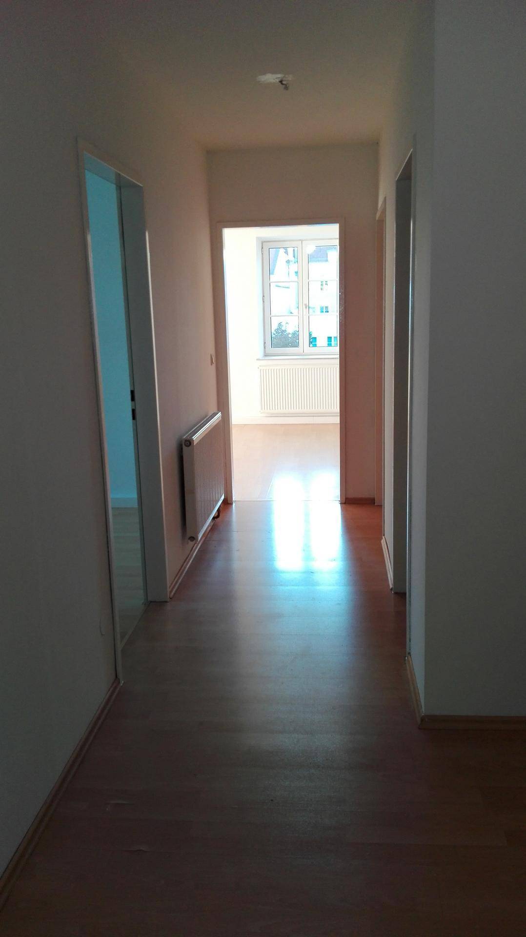 Langer, heller Flur mit Holzboden, der zu weiteren Zimmern und einem Fenster führt.