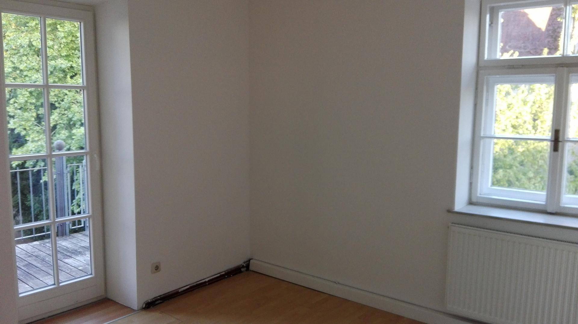 Leeres Zimmer mit Zugang zu einem Balkon oder einer Terrasse und Blick ins Grüne.