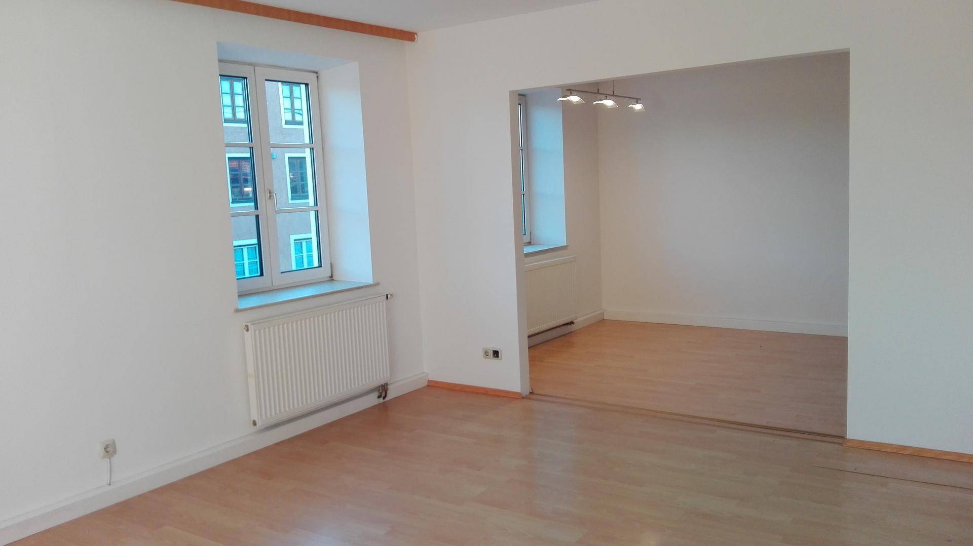 Offener Wohnbereich mit Holzboden und Fenstern, die den Raum mit Tageslicht füllen.