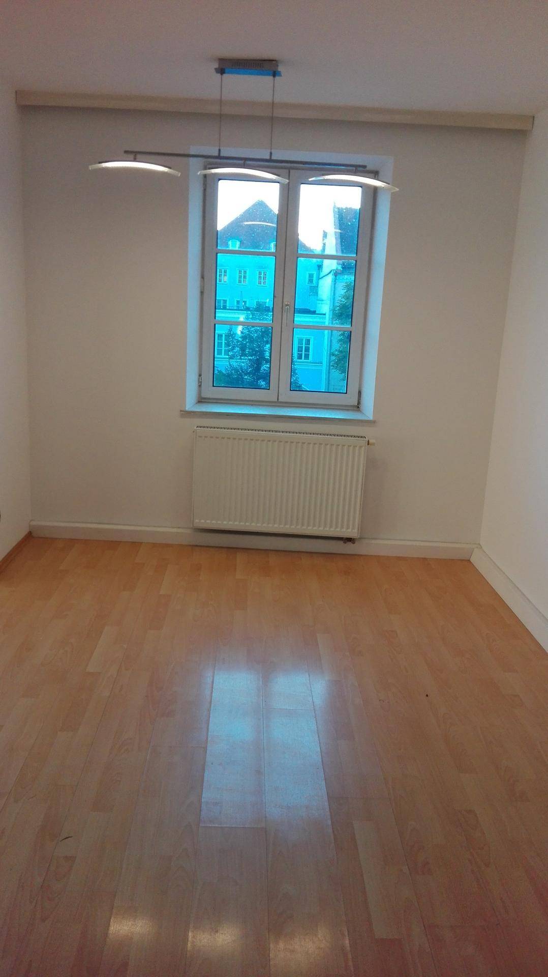 Helles Zimmer mit Holzboden und einem Fenster, das den Blick auf die Nachbarschaft freigibt.