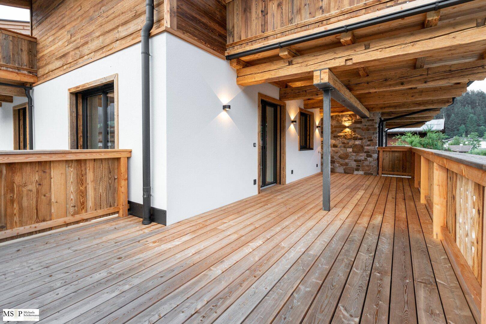 Großer Holzbalkon mit traditionellem Geländer und Holzbalkendecke, bietet viel Platz im Freien.