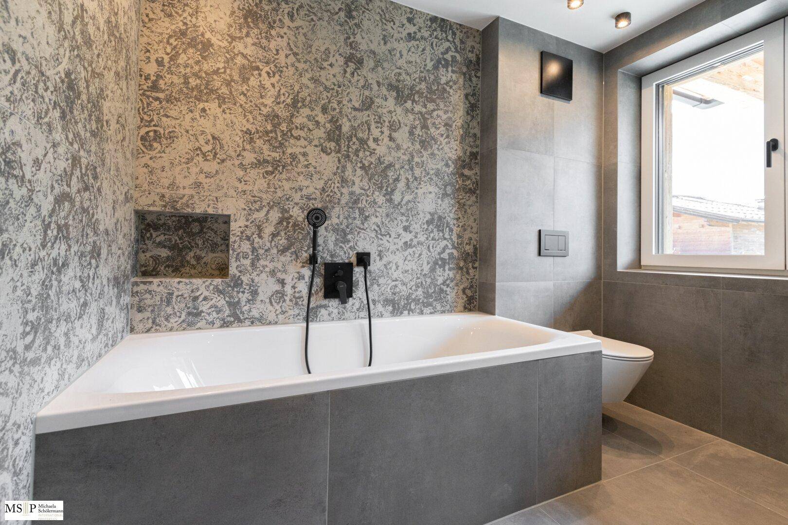 Stilvolles Badezimmer mit Badewanne und wandhängendem WC, ergänzt durch eine moderne Fliesenwand.