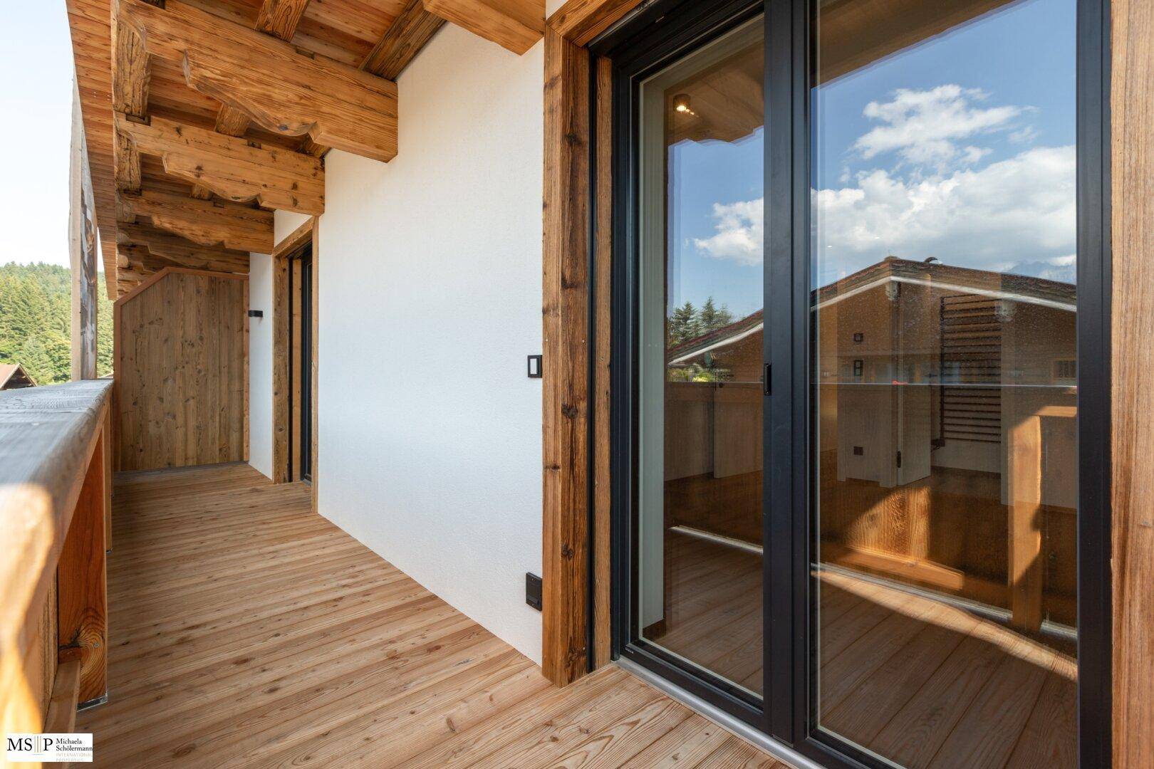 Heller Holzbalkon mit Blick auf die Umgebung und Zugang zu den Innenräumen durch eine Glasschiebetür.
