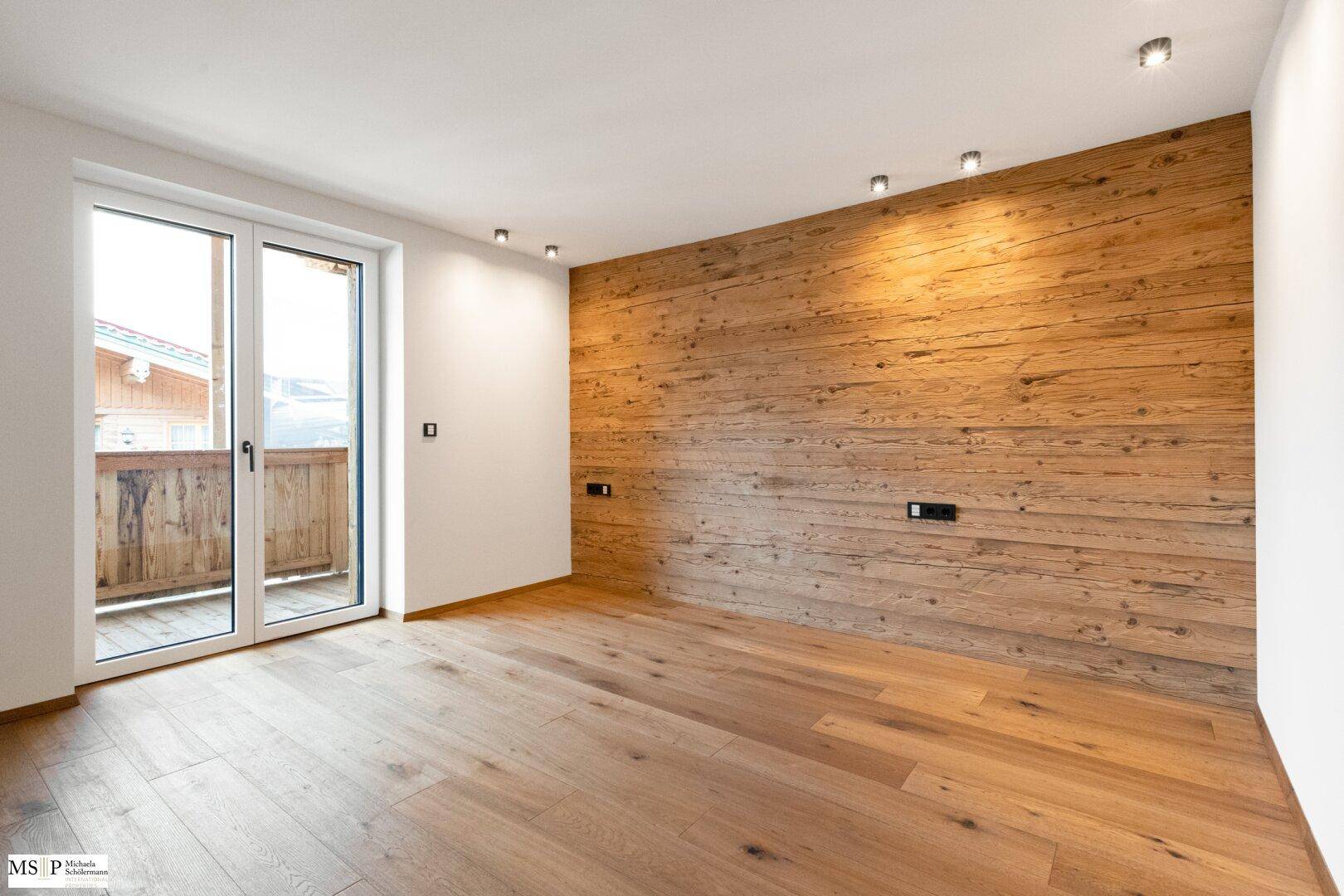Gemütliches Zimmer mit Holzboden, einer Akzentwand aus Holz und Balkonzugang, schafft eine warme Atmosphäre.