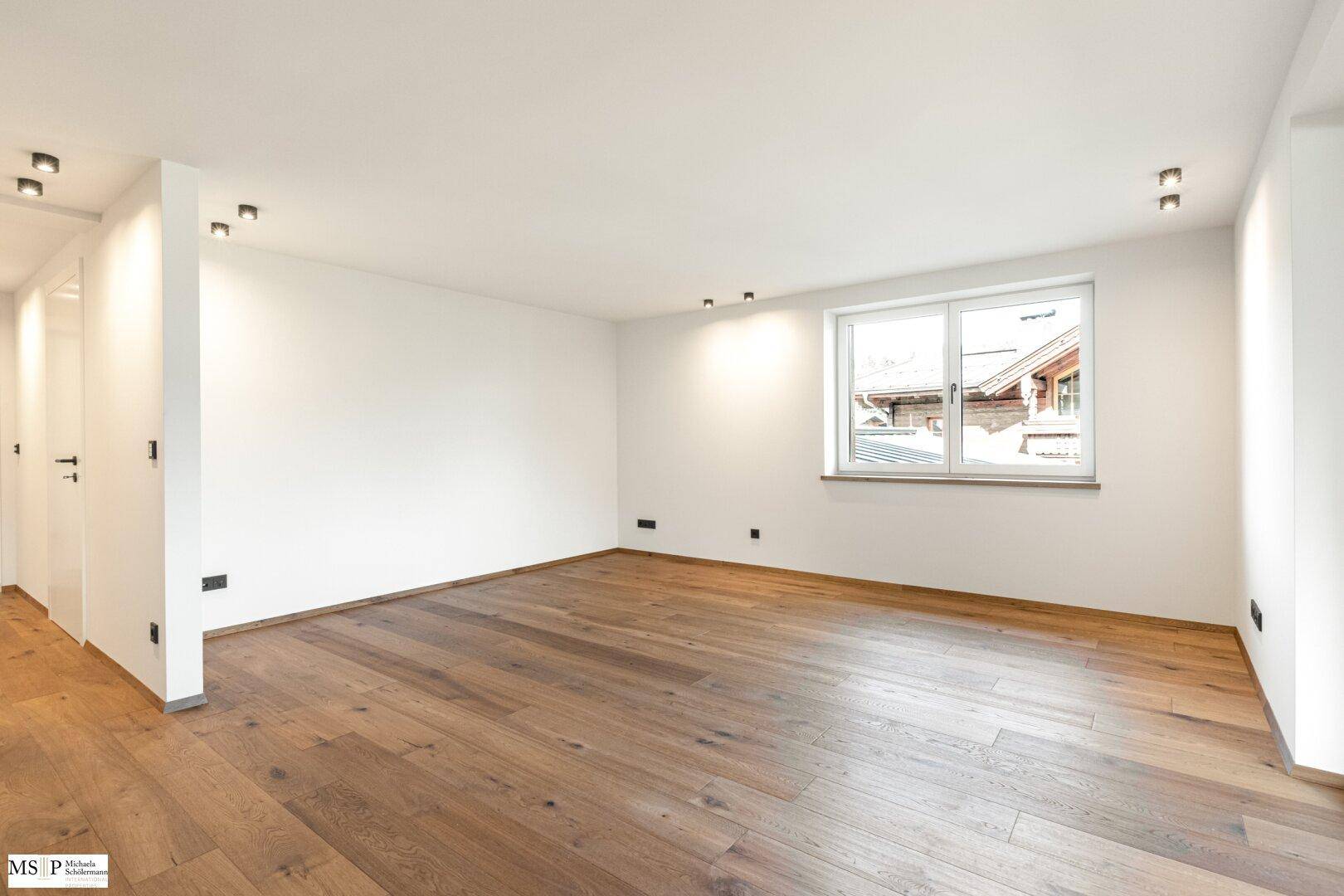 Geräumiges, helles Zimmer mit Holzboden und großem Fenster, bietet viel Tageslicht.
