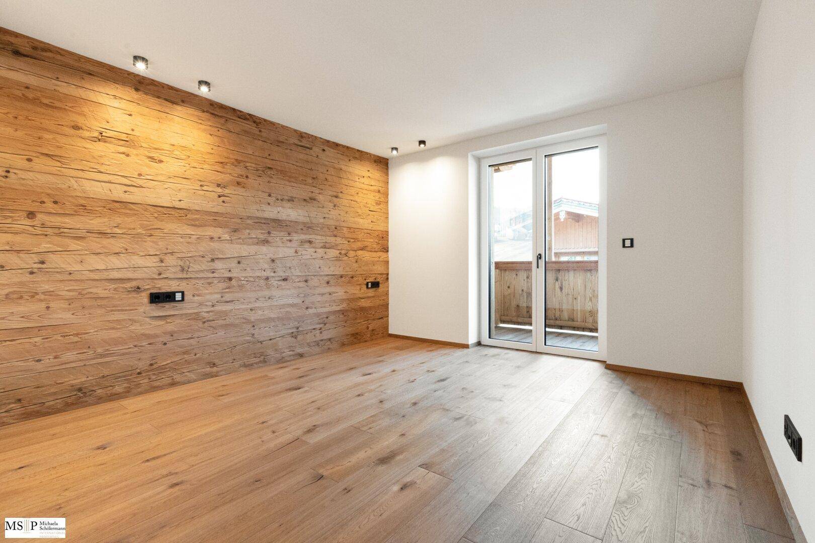 Helles Zimmer mit Holzboden und Holzwand, bietet direkten Zugang zu einem sonnigen Balkon.