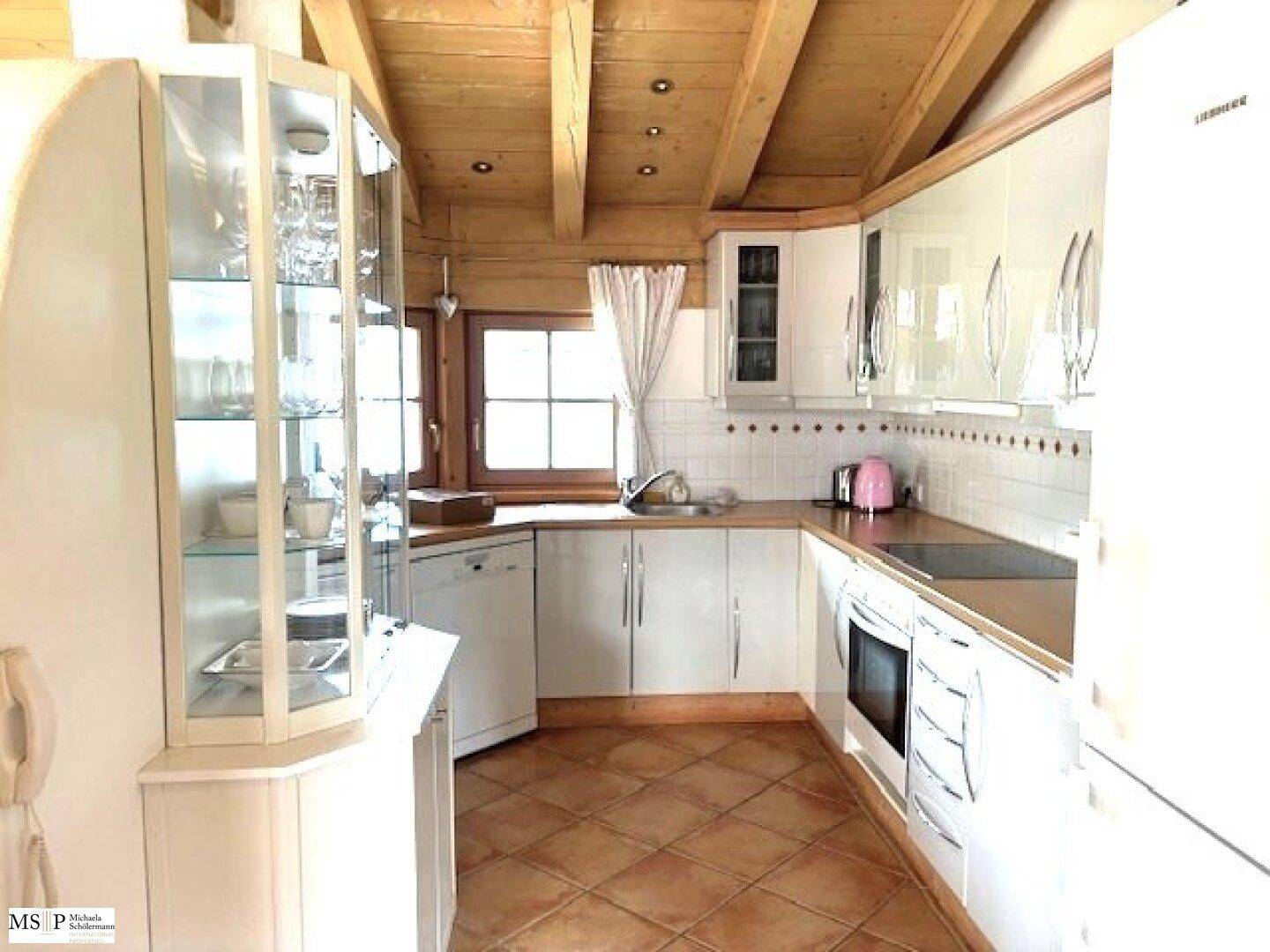 Helle Küche mit weißen Schränken, Holzbalkendecke und traditionellen Terrakottafliesen.