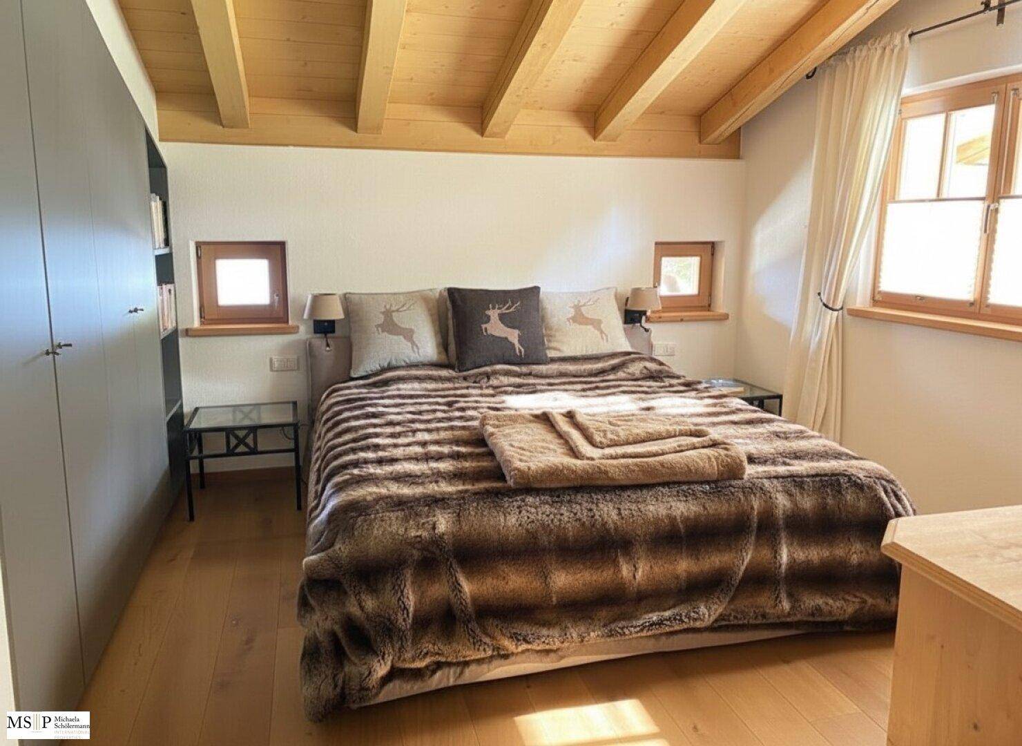 Gemütliches Schlafzimmer mit großem Bett, Holzbalkendecke und Holzboden im Landhausstil.