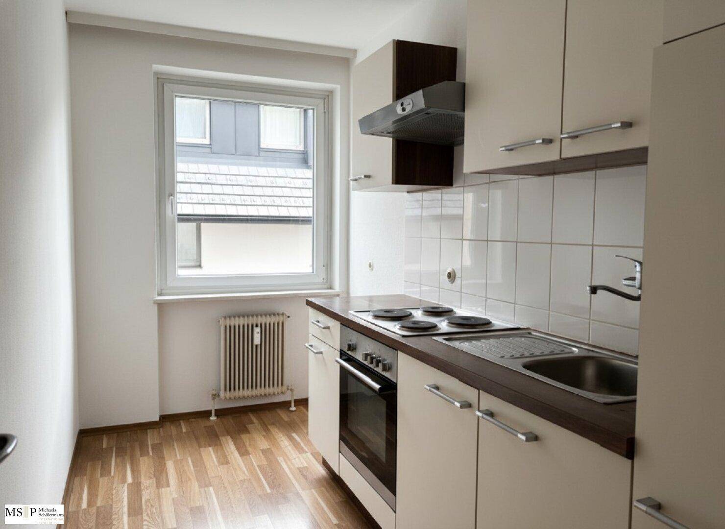 Kompakte Einbauküche mit Herd, Backofen und Spüle unter einem Fenster.