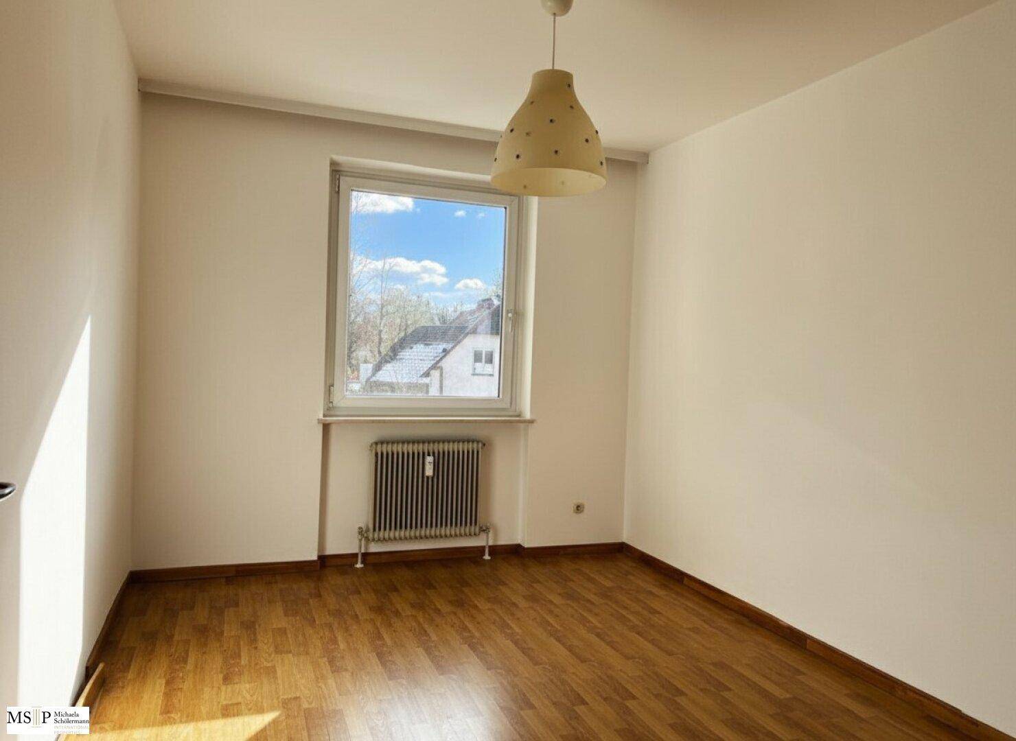 Helles Schlafzimmer mit Holzparkettboden, großem Fenster und Blick ins Grüne.