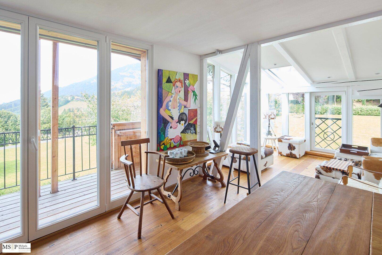 Heller Wohnbereich mit Holzboden, farbenfroher Kunst und Zugang zu einem Balkon mit Bergblick.