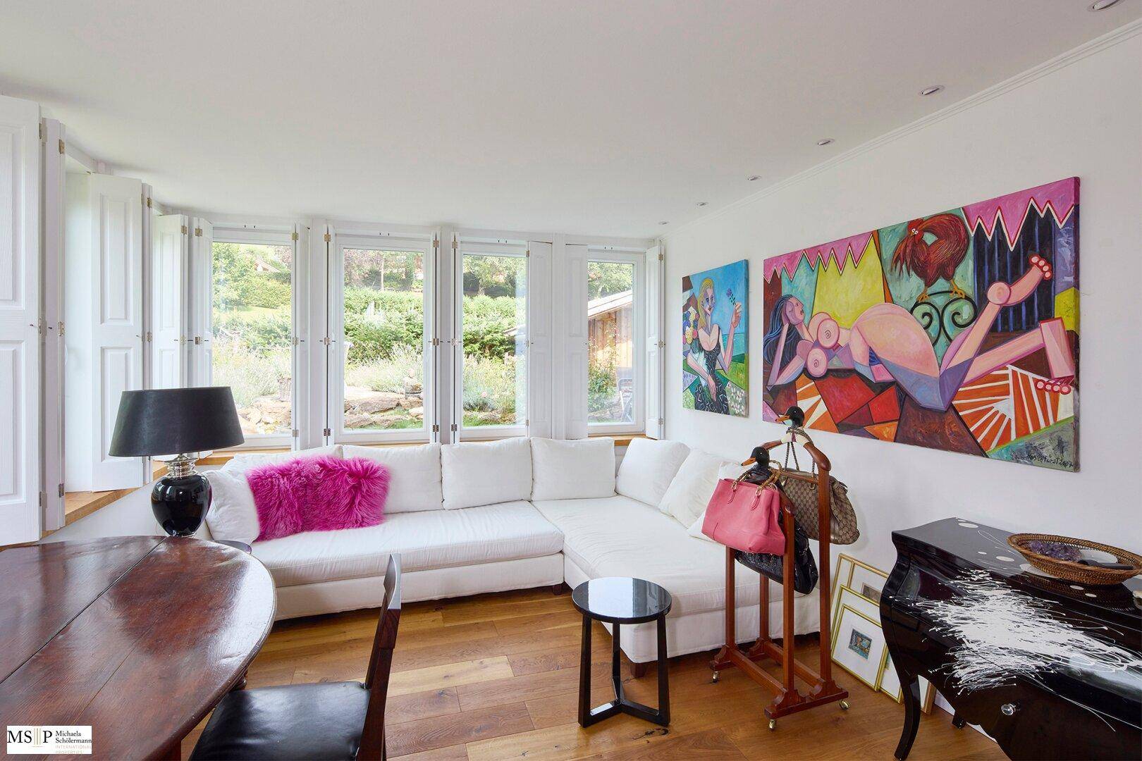 Moderner Wohnbereich mit weißem Sofa, farbenfroher Kunst und Holzboden.