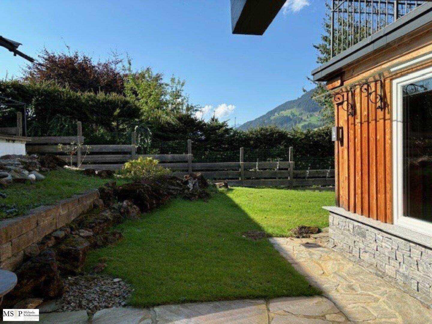 Gepflegter Gartenbereich mit Rasenfläche, Steinplatten und Blick auf die umliegenden Hügel.