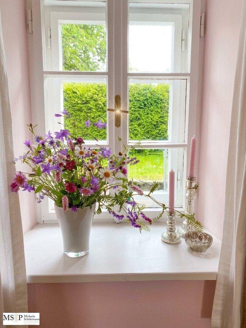 Helles Fenster mit frischen Blumen auf der Fensterbank und Blick ins Grüne.