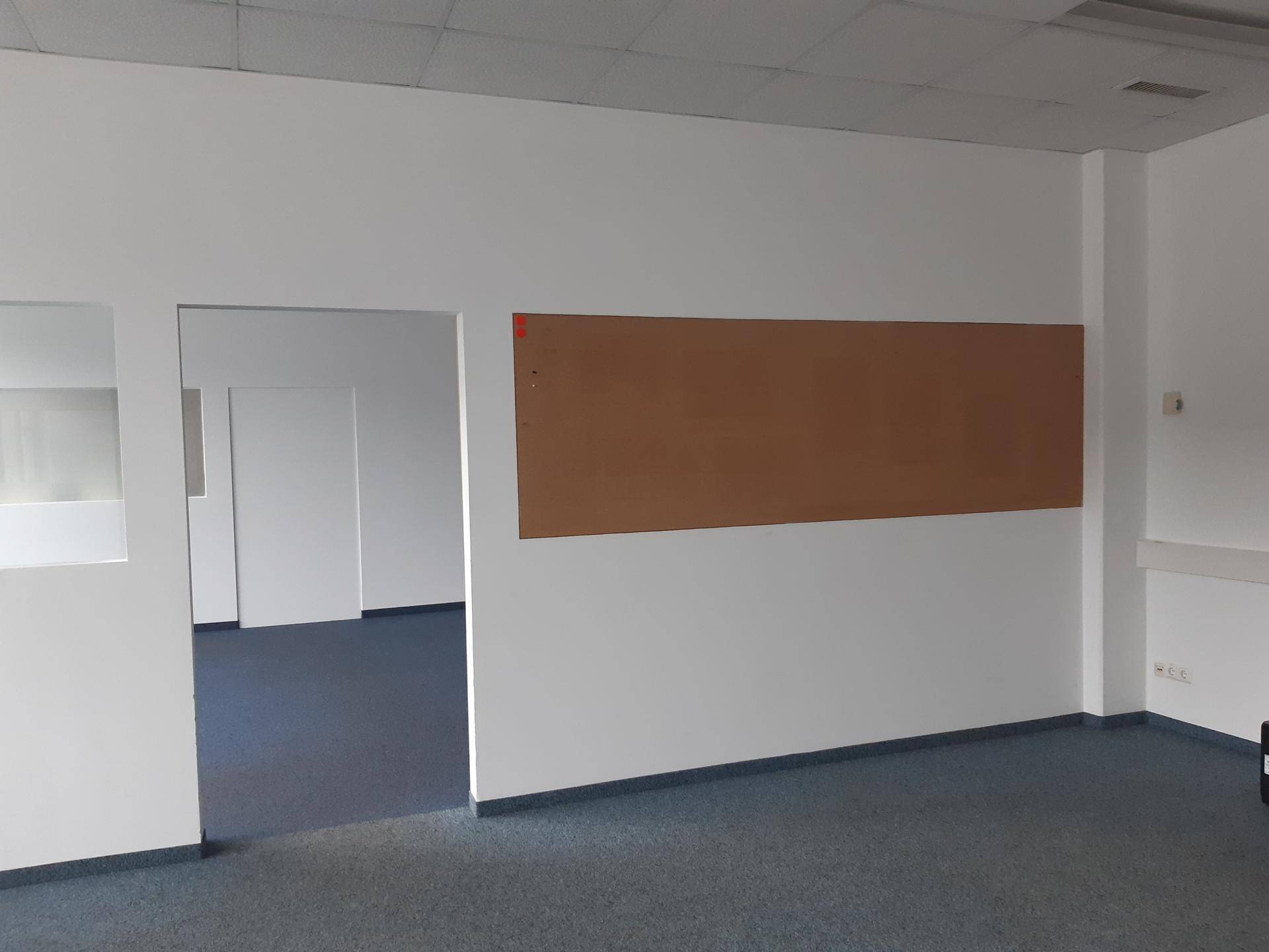 Innenansicht eines Büros mit weiß gestrichenen Wänden und einem braunen Anschlagbrett.