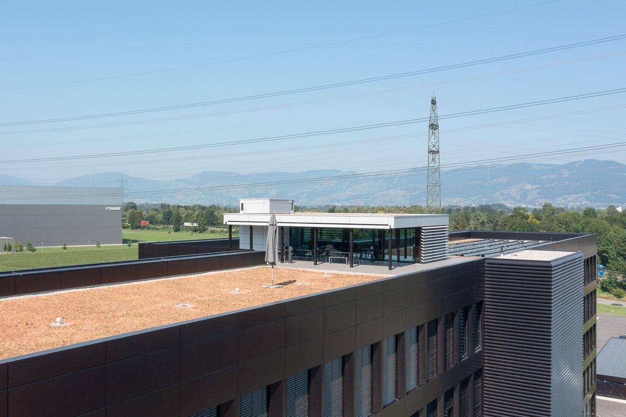 Dachterrasse mit Sitzgelegenheiten und begrüntem Dachbereich, umgeben von einer weiten Landschaft.