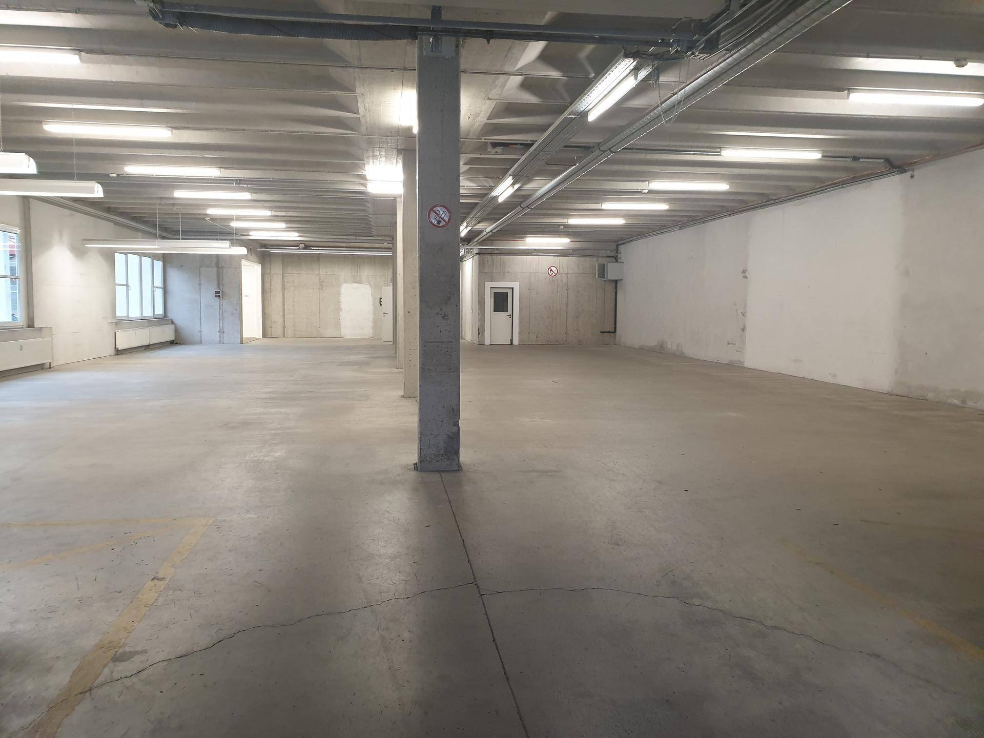 Großer, offener Gewerberaum mit Betonstützen und industrieller Beleuchtung, ideal für verschiedene Zwecke.