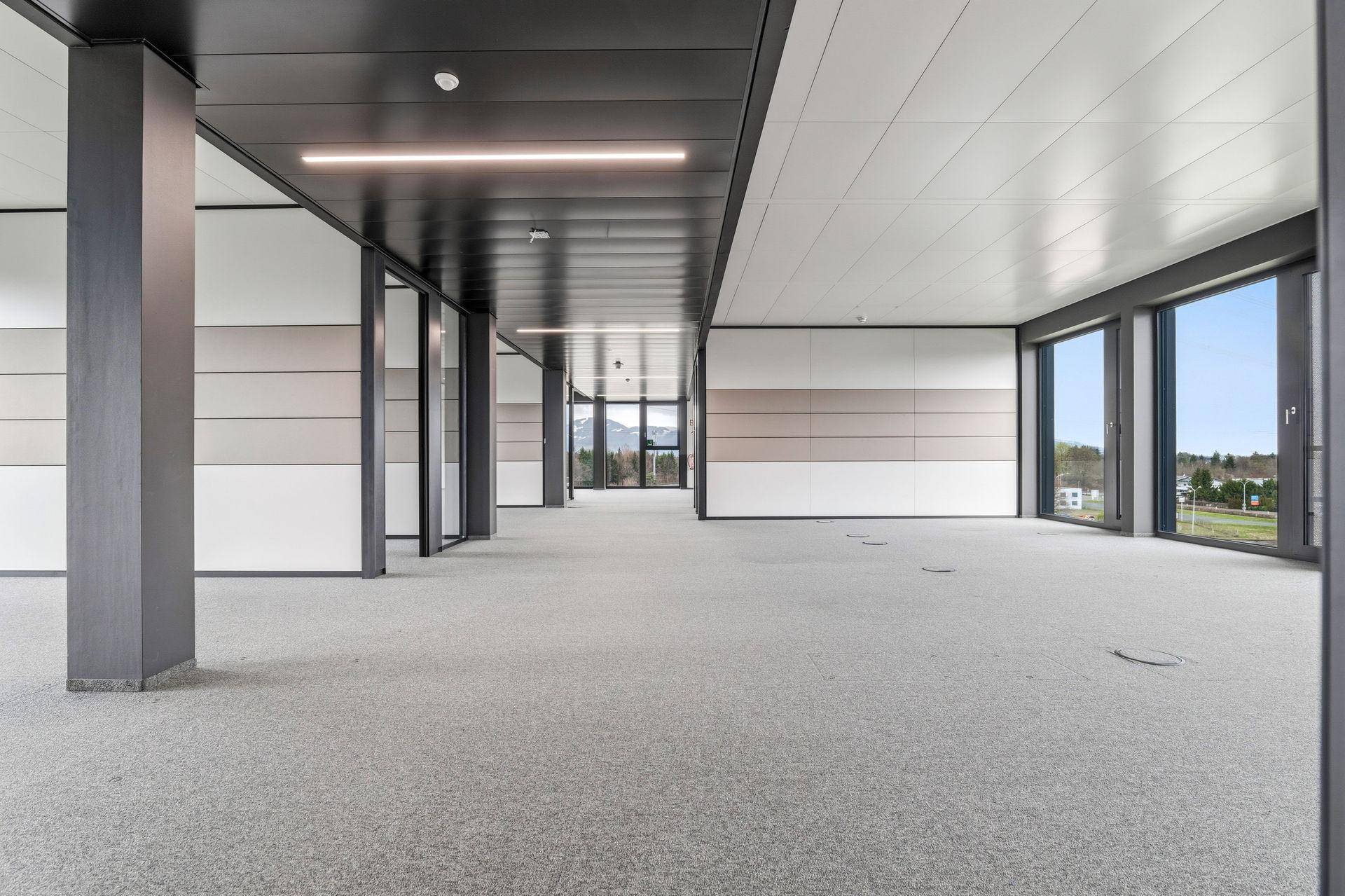 Weitläufiger, leerer Bürobereich mit Teppichboden und großen Fenstern, die einen Blick auf die Berge freigeben.