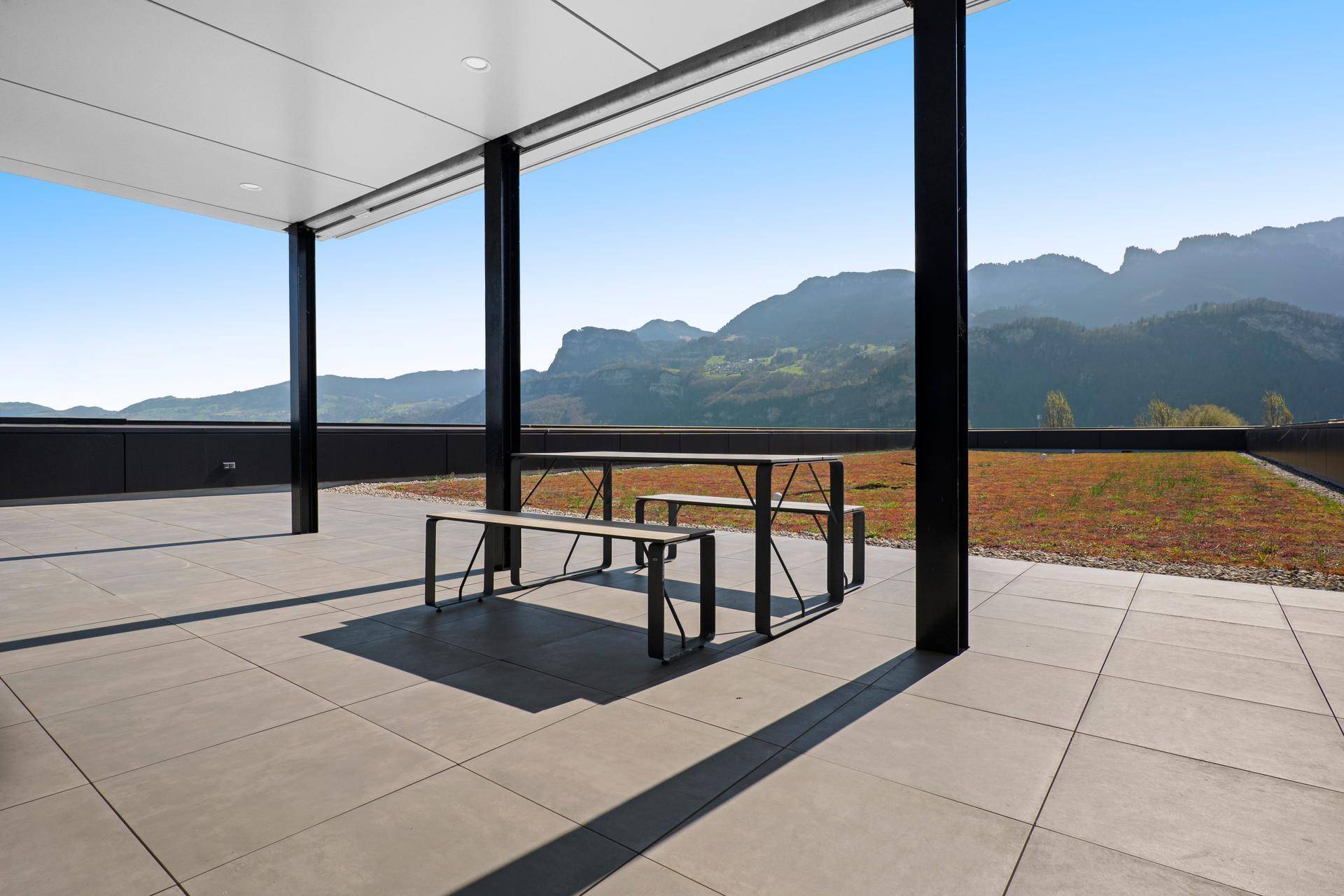 Geräumige Dachterrasse mit Sitzgelegenheiten, Fliesenboden und weitem Blick auf die Berge.