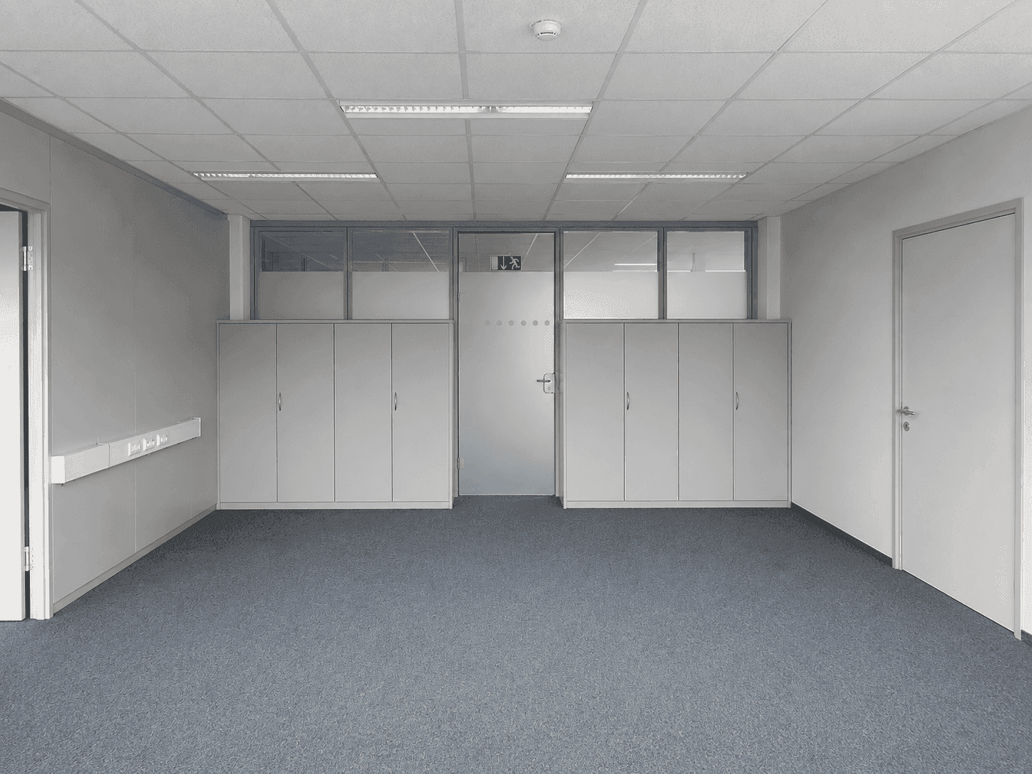 Bürofläche mit Teppichboden, Einbauschränken, einer Glastür und praktischer Deckenbeleuchtung.
