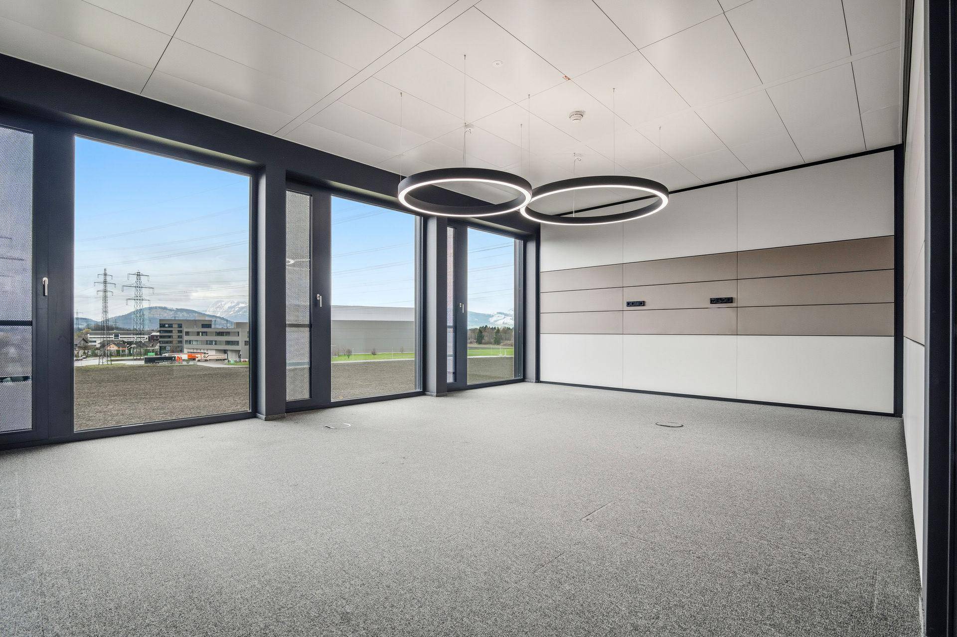 Geräumiger, leerer Büroraum mit großen Fenstern, die einen weiten Blick auf die Landschaft und Berge bieten.
