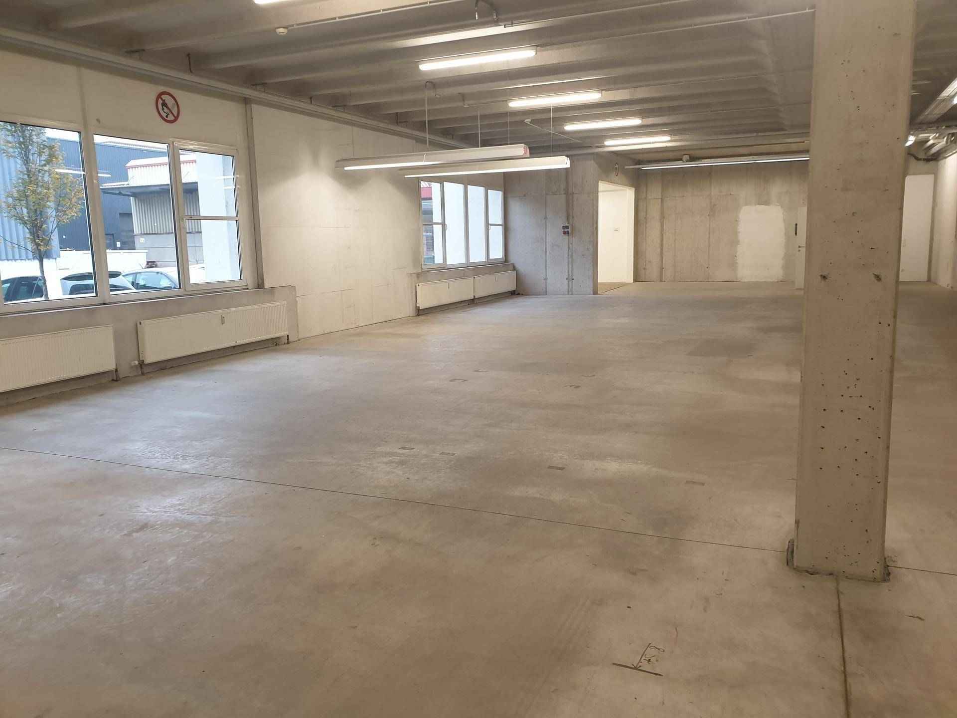 Geräumiger, unmöblierter Gewerberaum mit Betonstützen und großen Fenstern für viel Tageslicht.