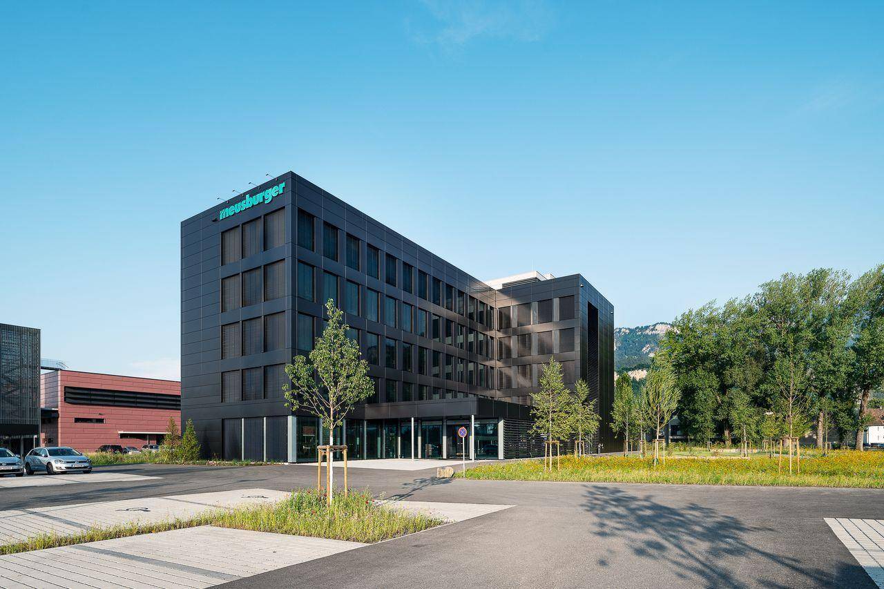 Ansicht des modernen Bürogebäudes mit dunkler Fassade und gepflegter Außenanlage unter klarem Himmel.