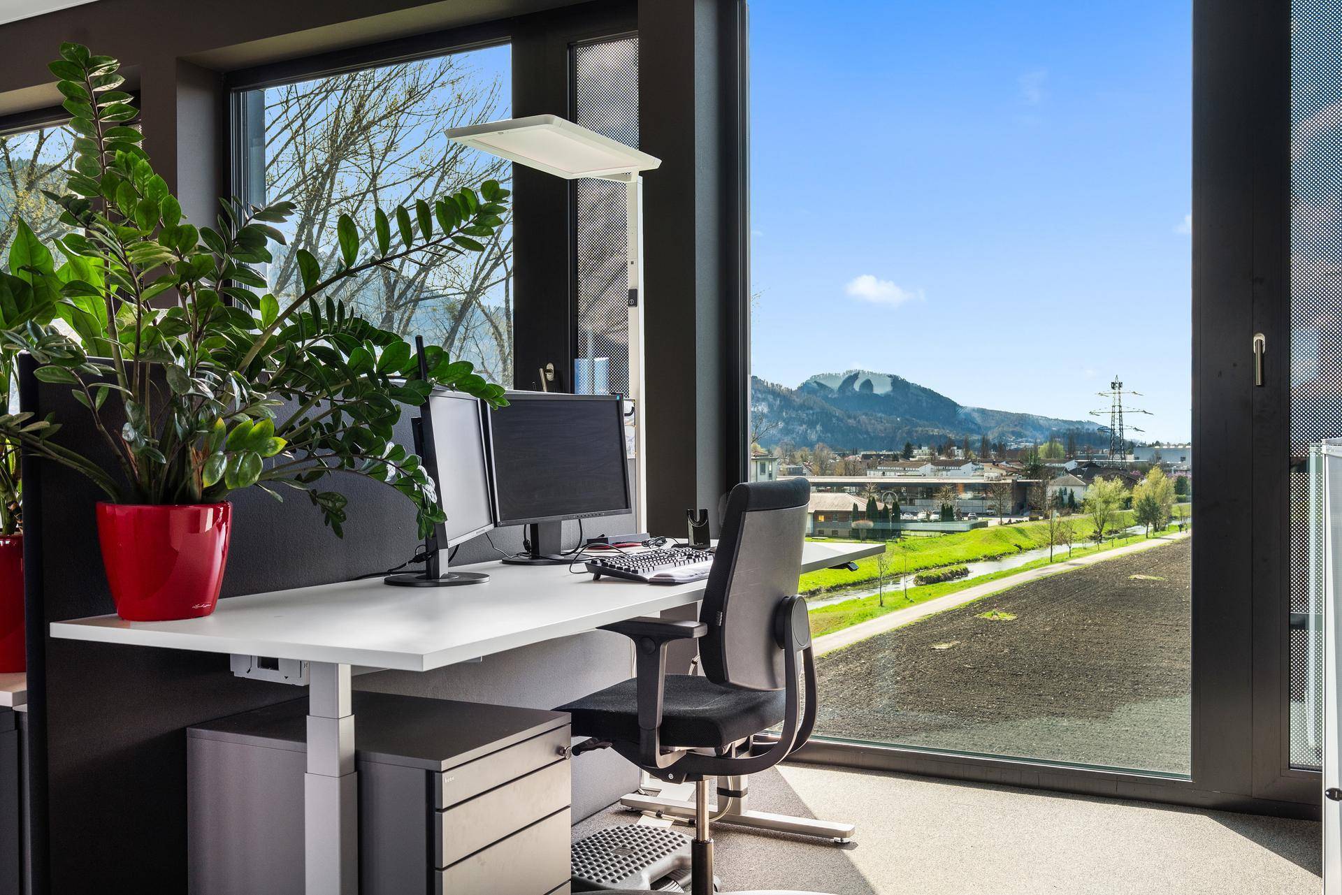 Modernes Büro mit großem Fenster, das einen weiten Blick auf die Berge und die grüne Landschaft bietet.