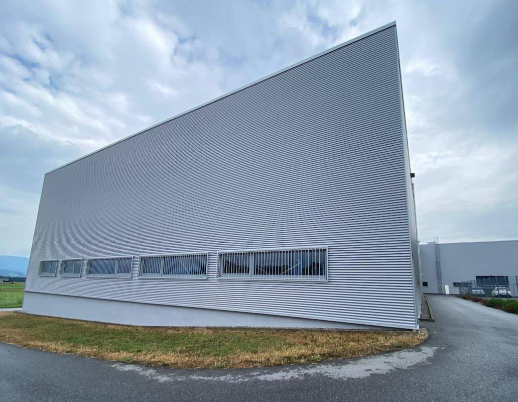 Seitenansicht eines modernen Industriegebäudes mit geriffelter Fassade und horizontalen Fensterbändern.