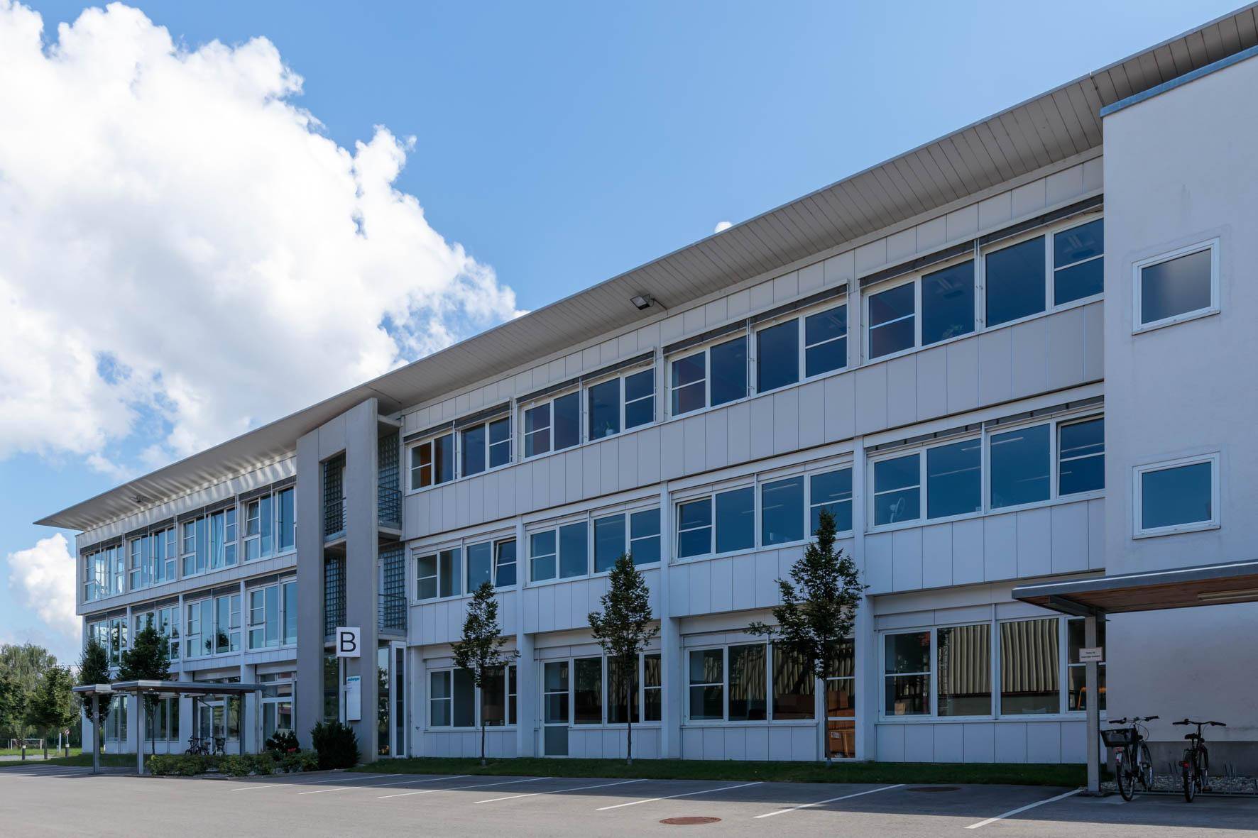 Ansicht eines modernen Bürokomplexes mit großen Fensterfronten und einem Parkplatz.