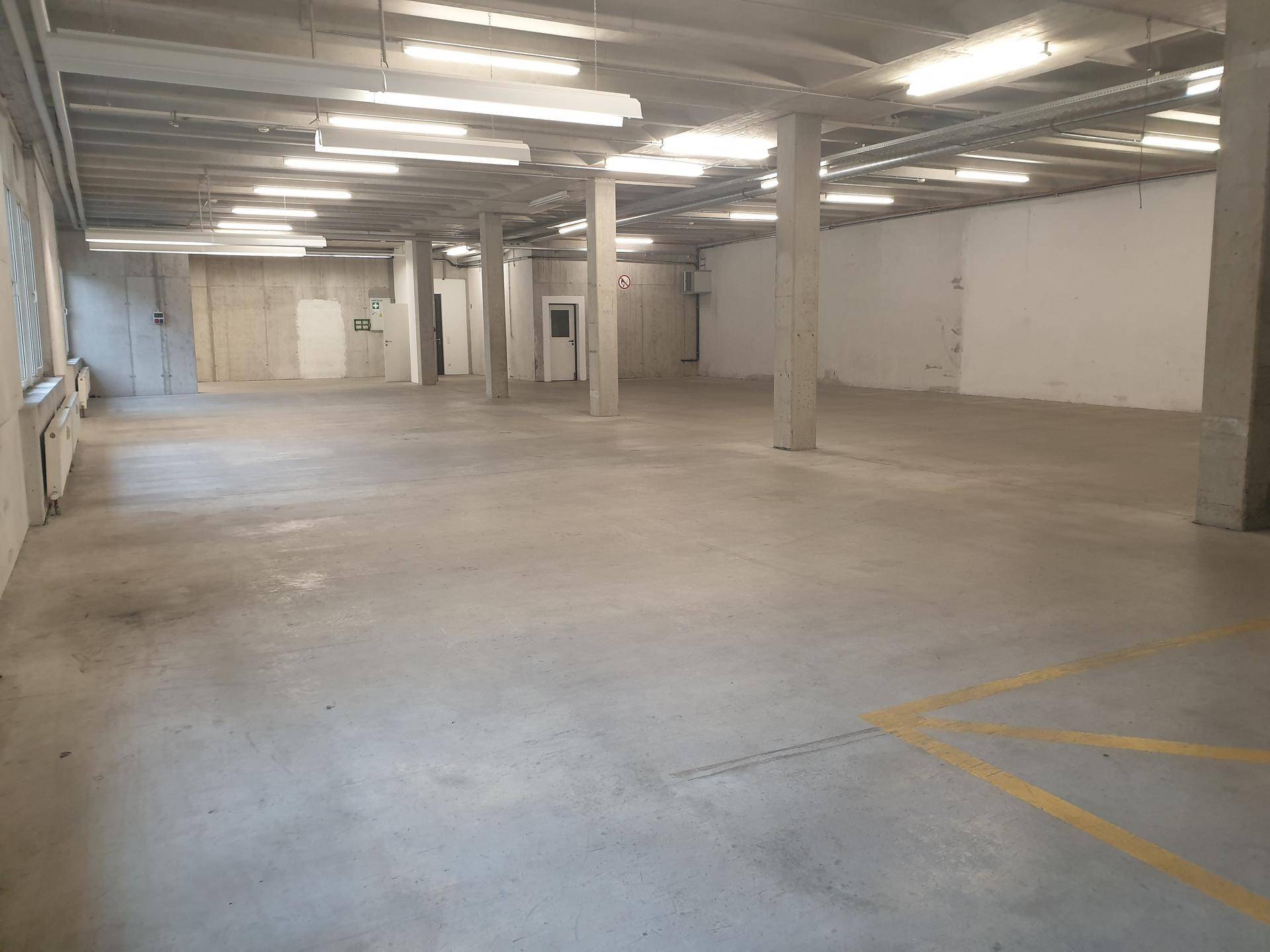 Heller, weitläufiger Gewerberaum mit Betonboden und sichtbaren Deckeninstallationen, bereit zur Nutzung.