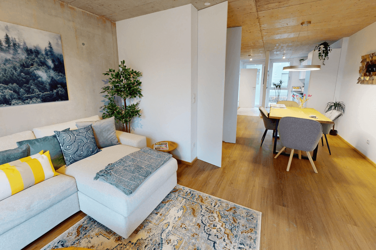 Offener Wohn- und Essbereich mit bequemer Couch, Esstisch und Holzboden.