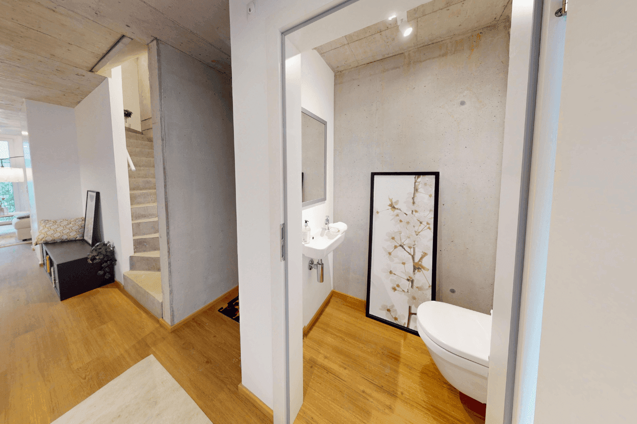 Gäste-WC mit modernem Wand-WC, Waschbecken und Sichtbetonwand.