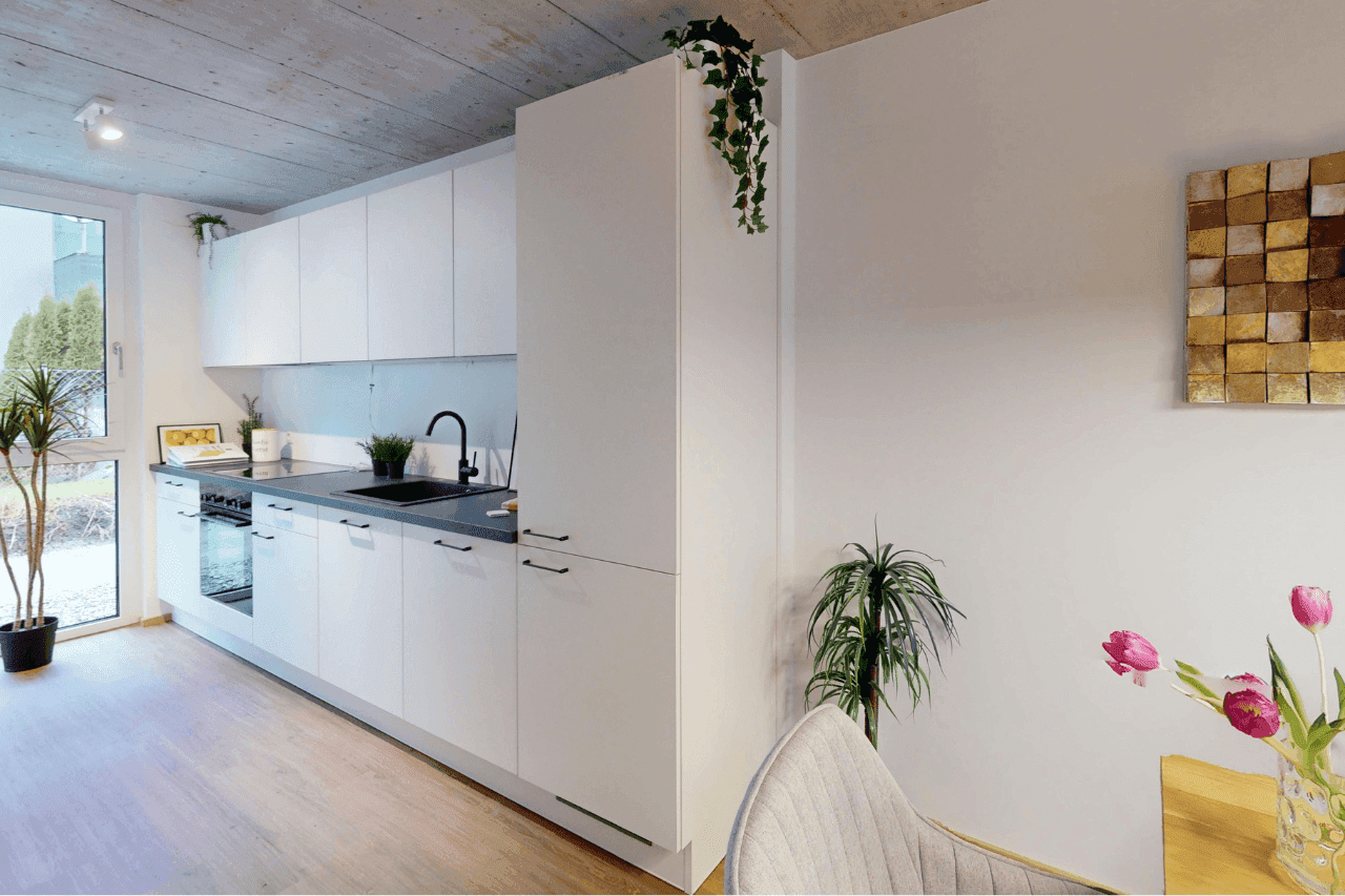 Moderne weiße Küche mit dunkler Arbeitsplatte, integrierten Geräten und Fenster.