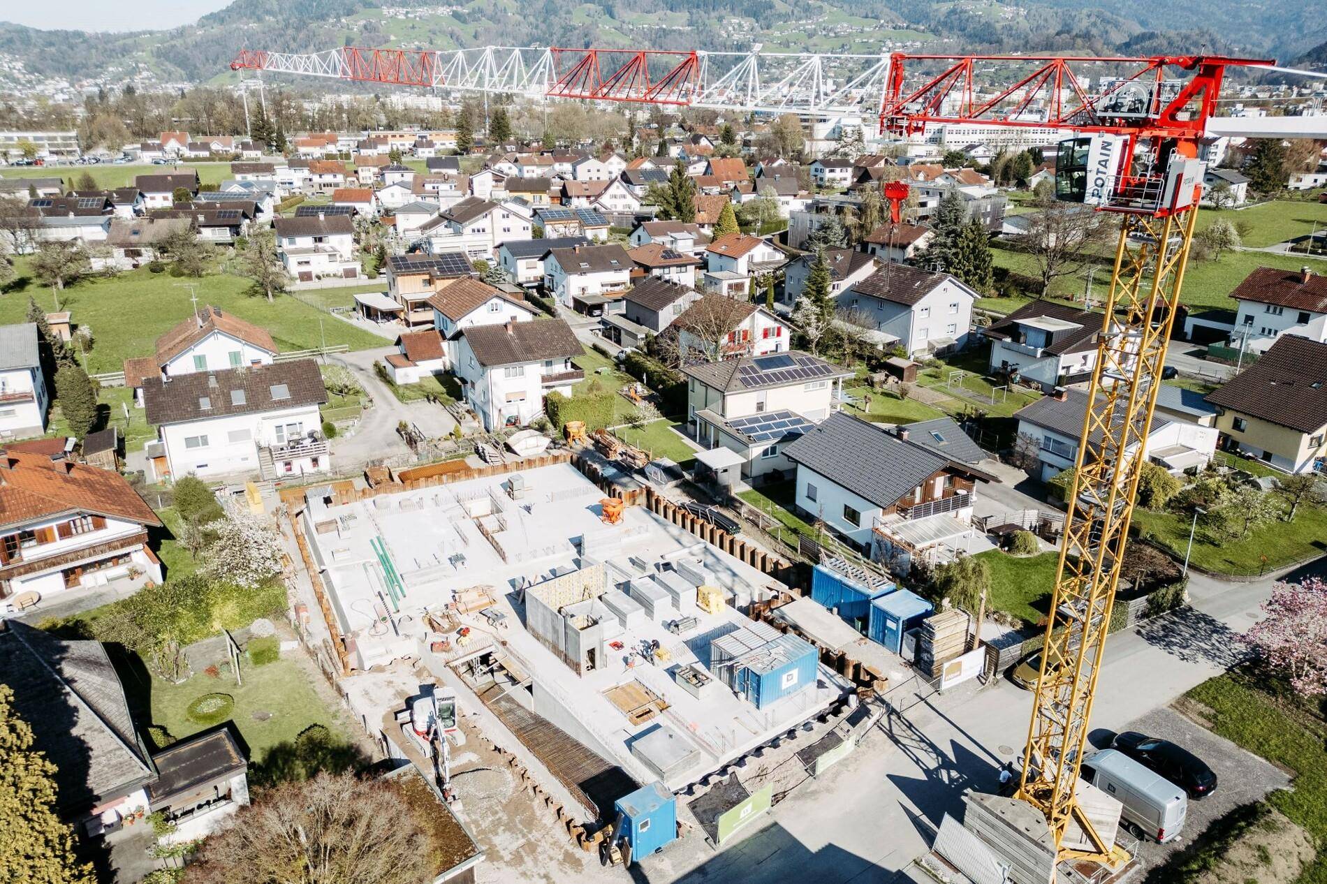 Luftaufnahme einer Baustelle mit Kran in einem Wohngebiet, umgeben von bestehenden Häusern.