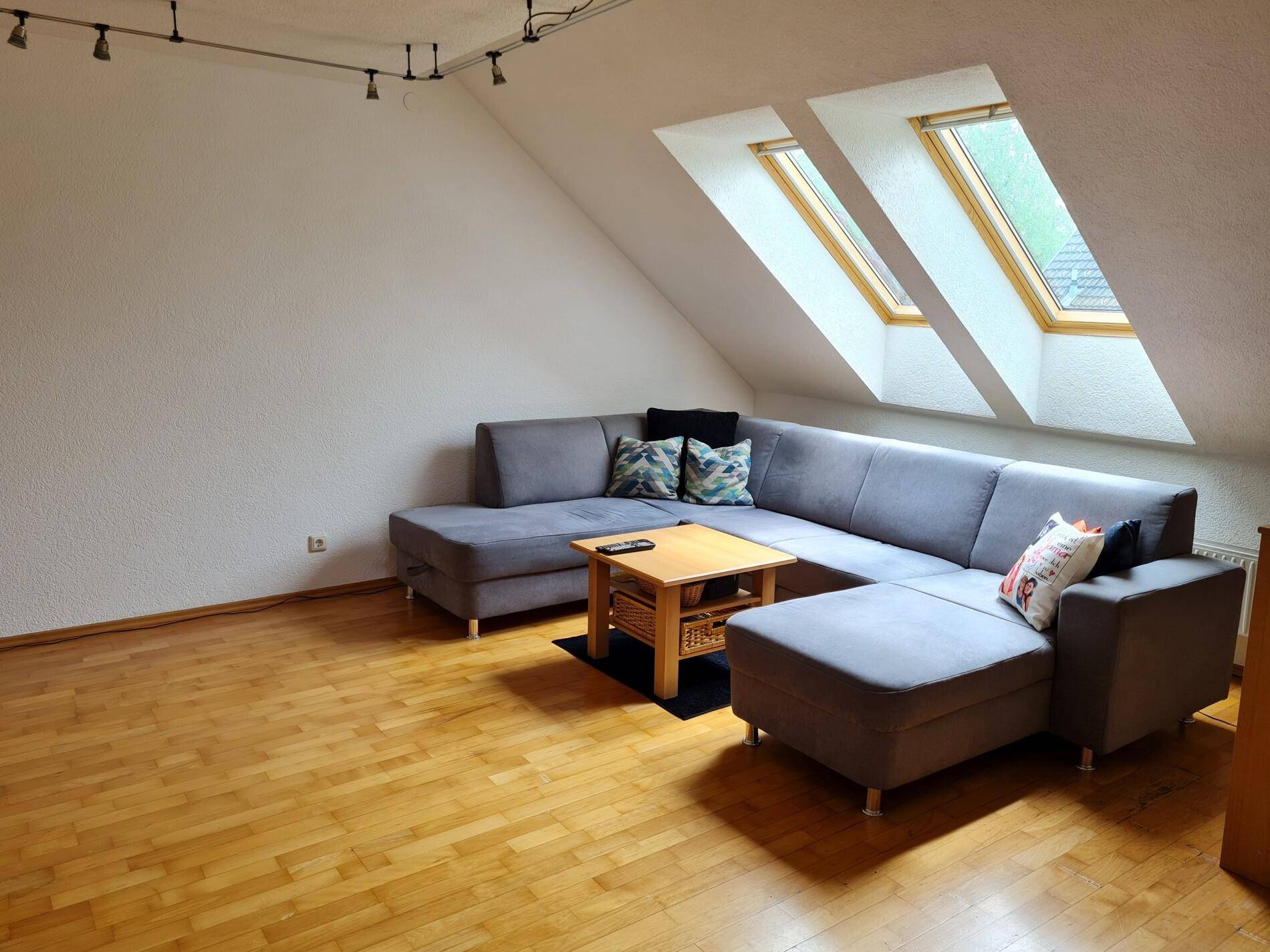 Gemütliches Wohnzimmer im Dachgeschoss mit schrägen Decken, großem Sofa und zwei Dachfenstern.